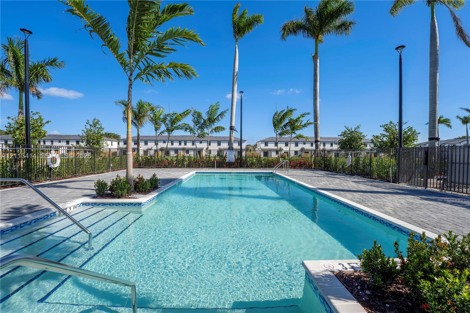 Rectangular swimming pool featuring a paved pool deck, perimeter metal fencing, integrated entry steps, and mature palm trees