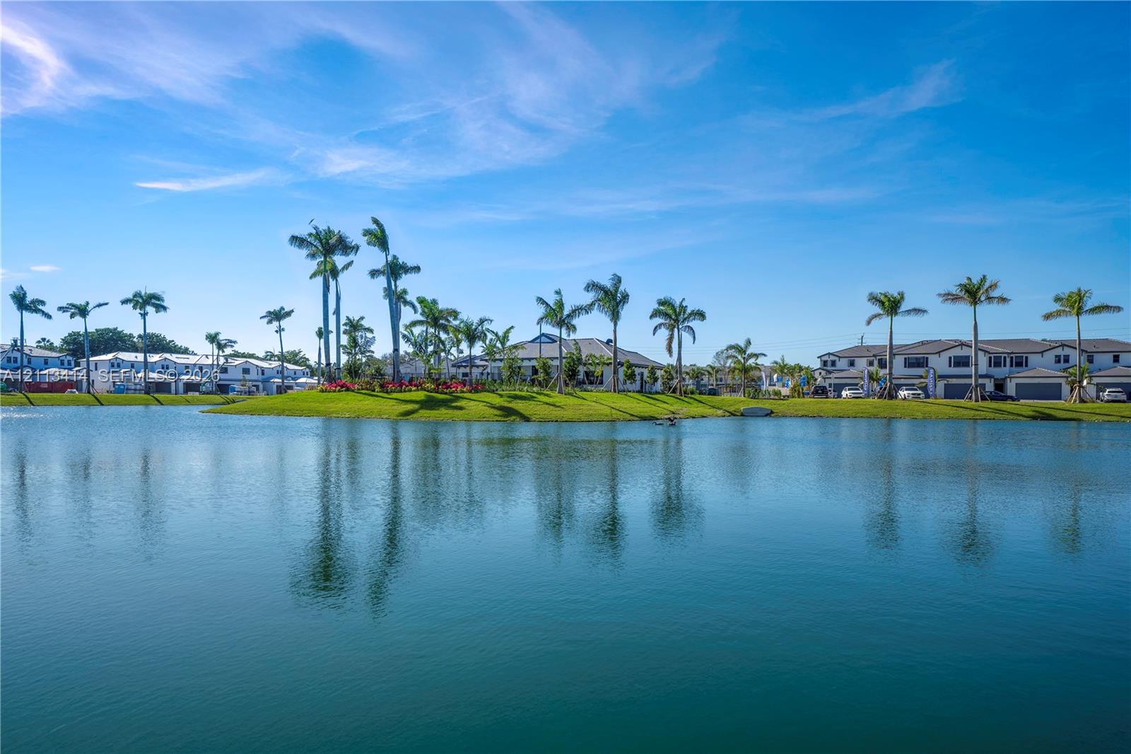 Waterfront property featuring a serene lake, manicured landscaping, and mature palm trees