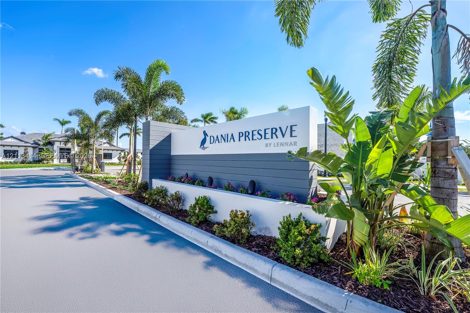 Community entrance featuring custom signage, horizontal wood-panel detailing, concrete curbing, and professional tropical landscaping