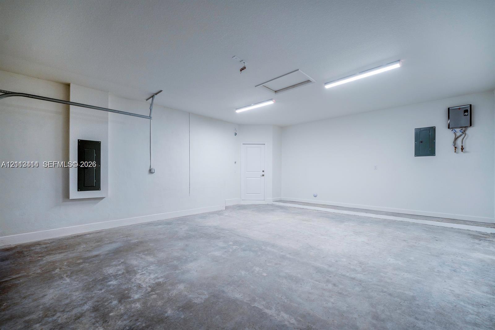 Finished garage featuring smooth walls, concrete flooring, dual overhead LED lighting fixtures, and an attic access panel