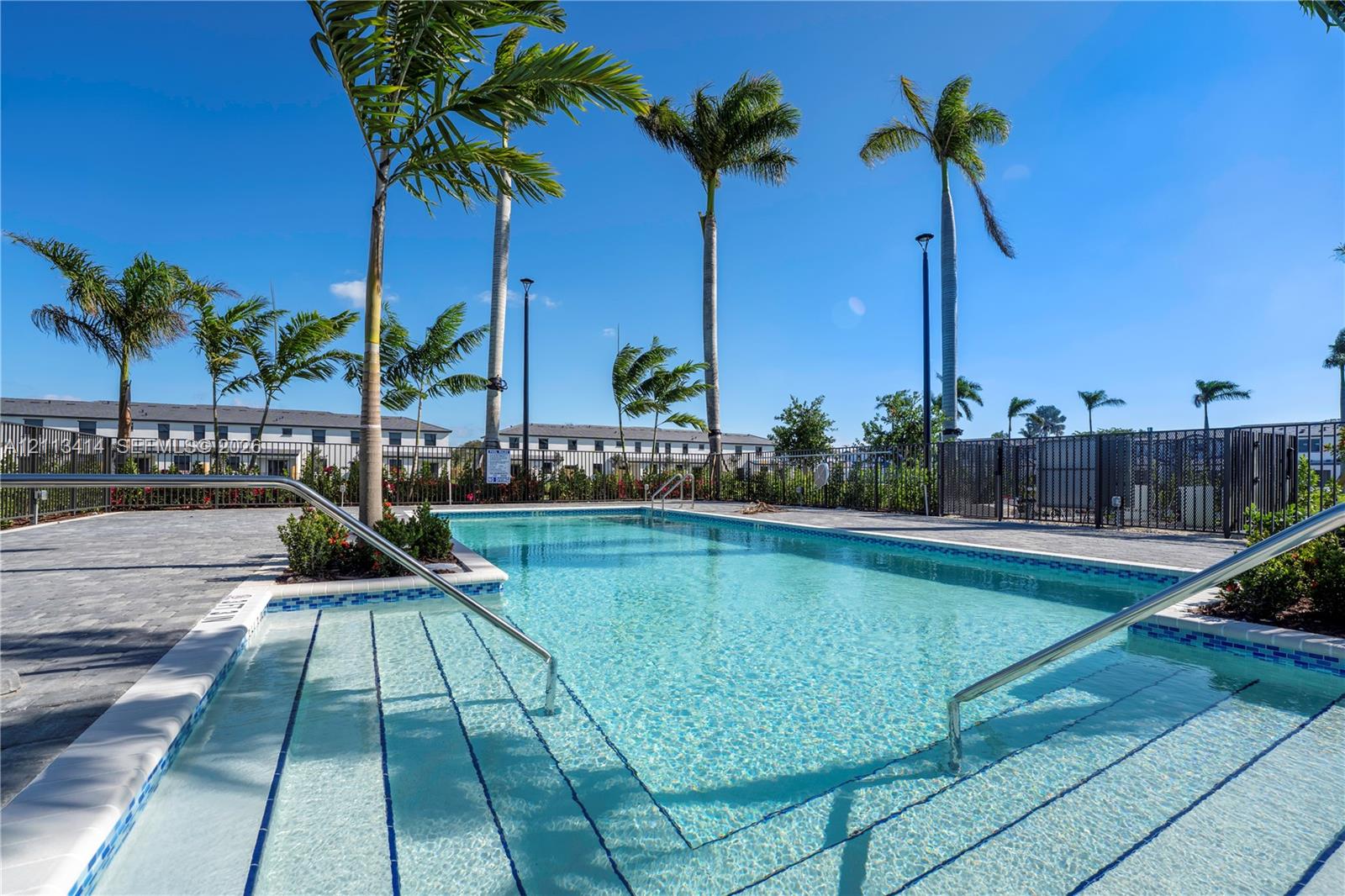 Swimming pool featuring stepped entry, stainless steel handrails, perimeter pavers, and mature palm trees