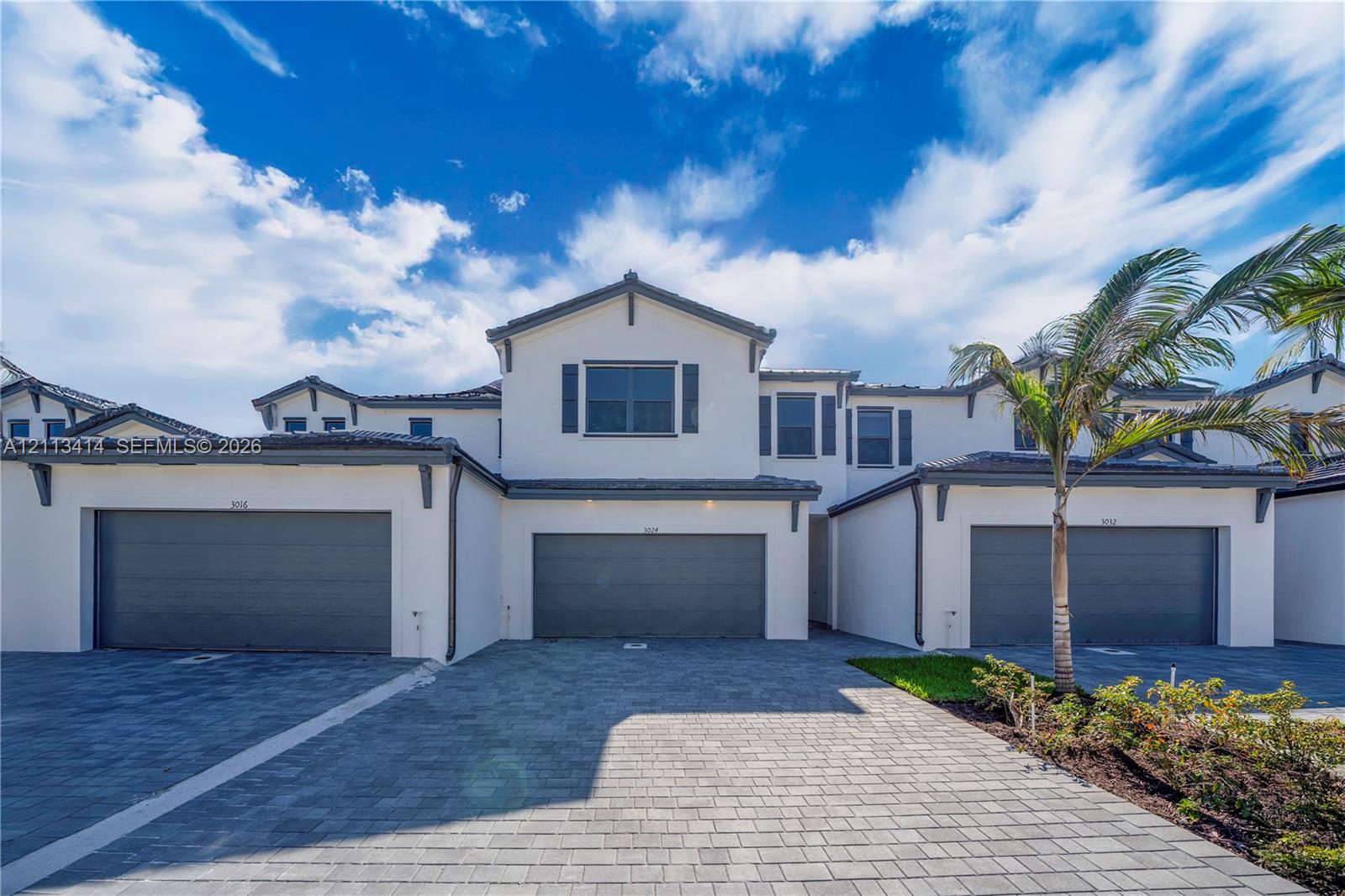 Multi-level stucco exterior featuring a tiled roof, grey-toned garage doors, and paver driveway