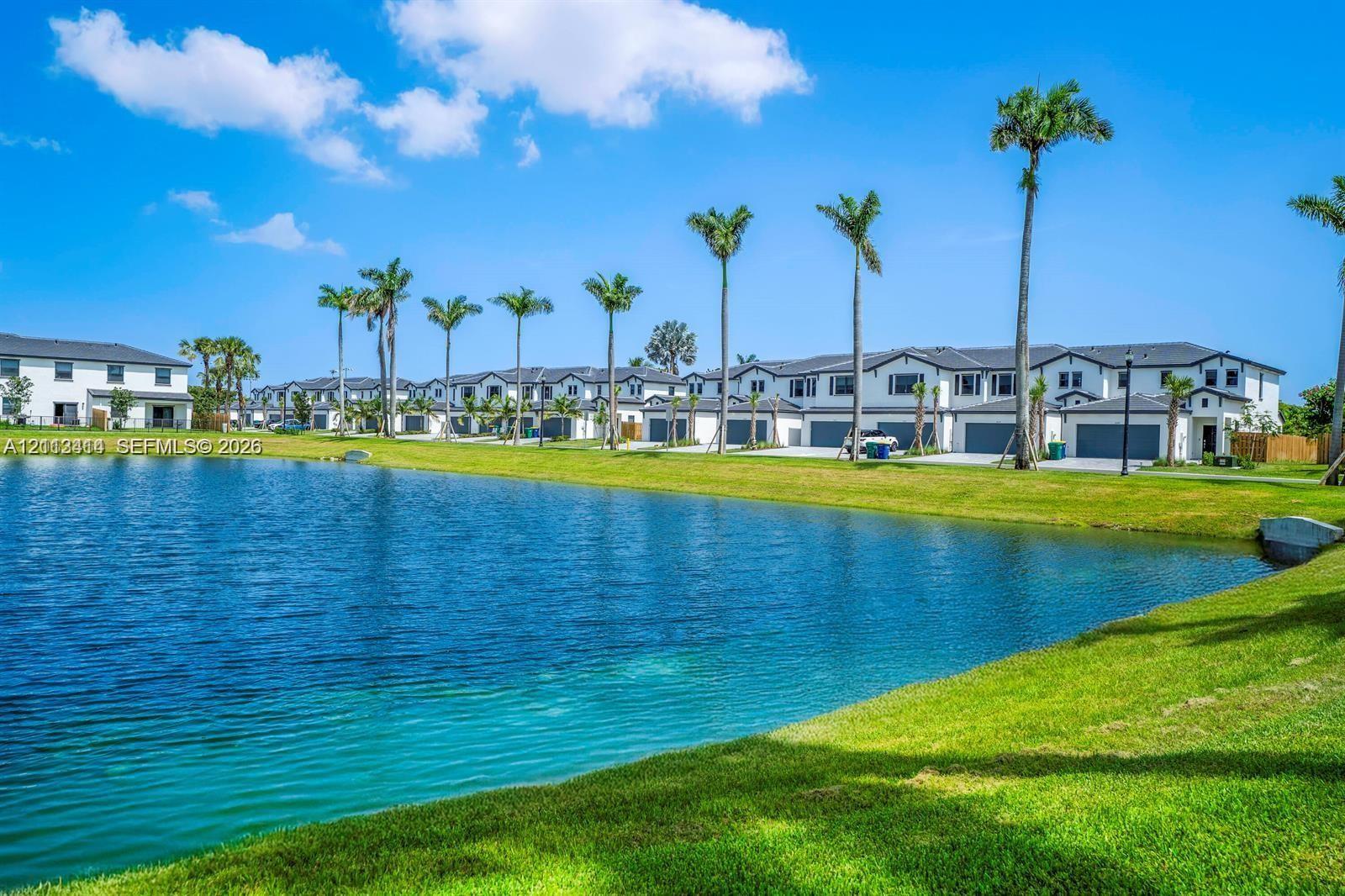 Waterfront exterior featuring a manicured lawn, established palm trees, and multi-unit residential structures with attached garages