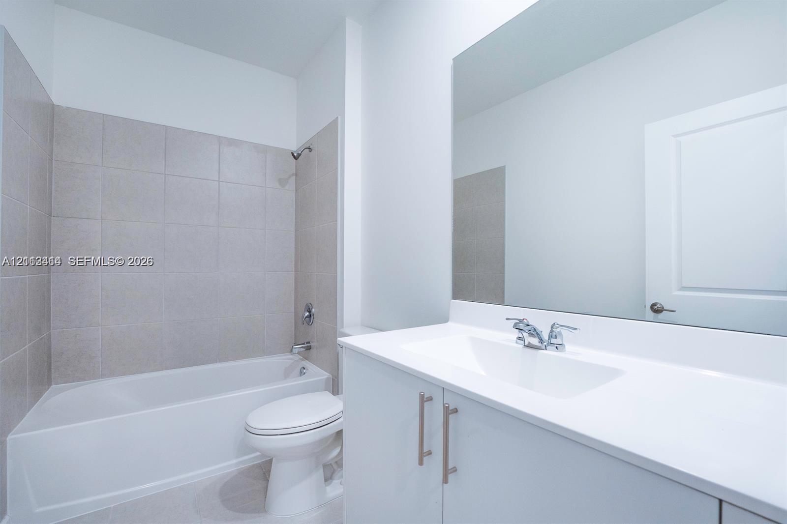 Bathroom featuring a white vanity cabinet with a solid surface countertop, an undermount sink with chrome fixtures, a full-width wall mirror, and a tile-surround bathtub