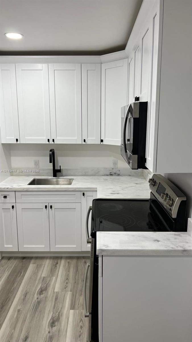 Kitchen featuring white Shaker-style cabinetry, light stone-finish countertops, stainless steel appliances, a matte black faucet, and wood-finish flooring