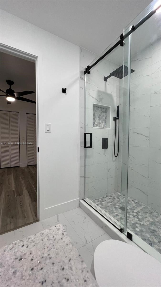 Walk-in shower featuring a glass enclosure with a matte black sliding track, rainfall showerhead, integrated tiled niche, and stone mosaic flooring