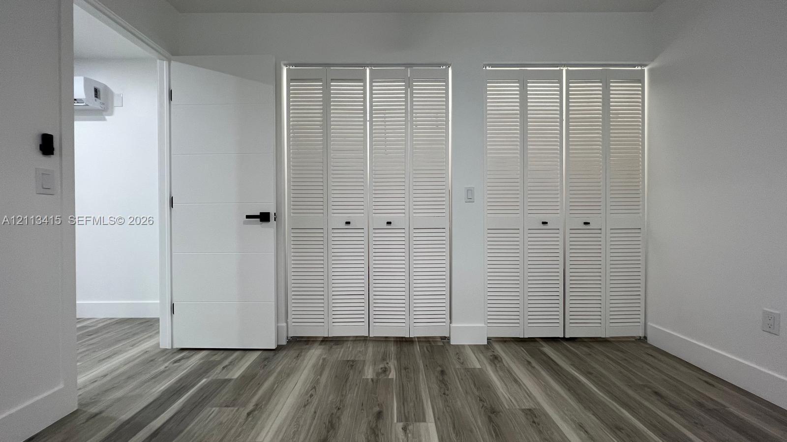 Wood-finish flooring, dual white louvered closet doors, and solid-core interior door with matte black hardware