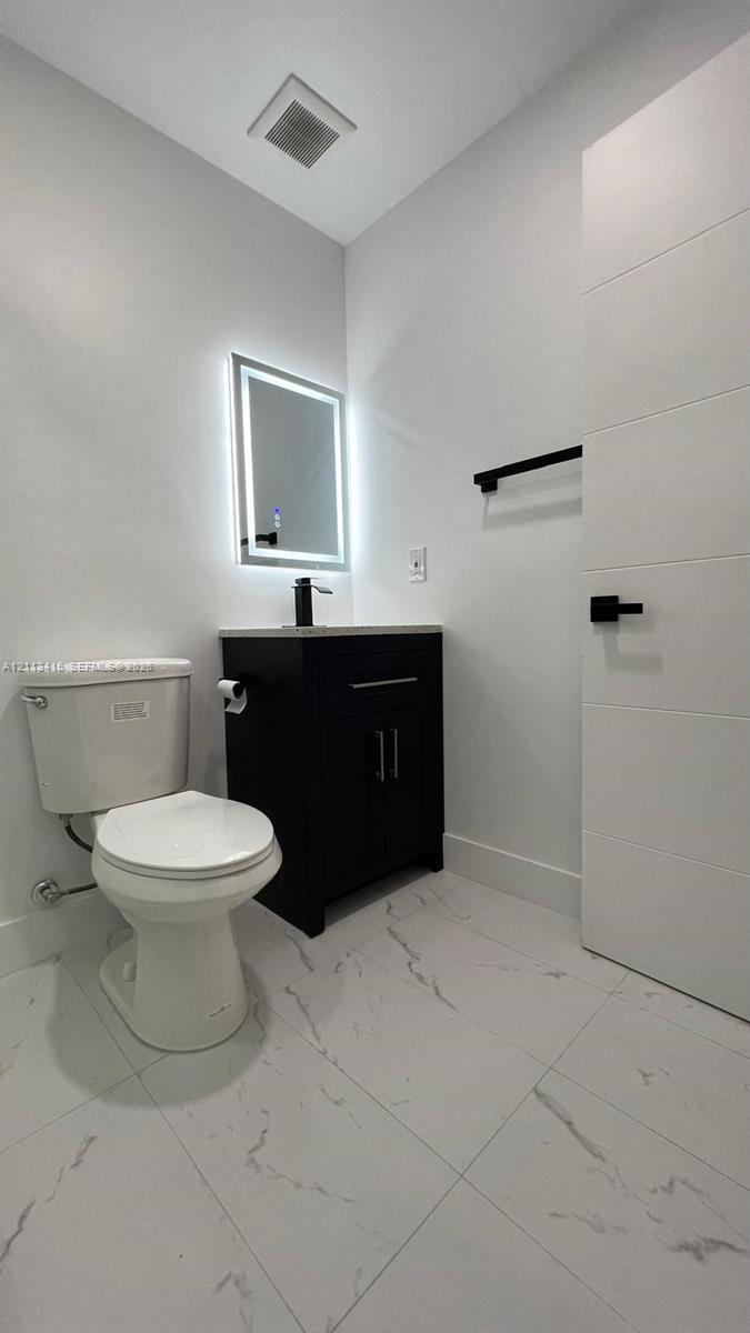 Modern bathroom featuring white tile flooring with grey veining, a dark-finish vanity with a stone countertop, a wall-mounted LED mirror, and matte black fixtures