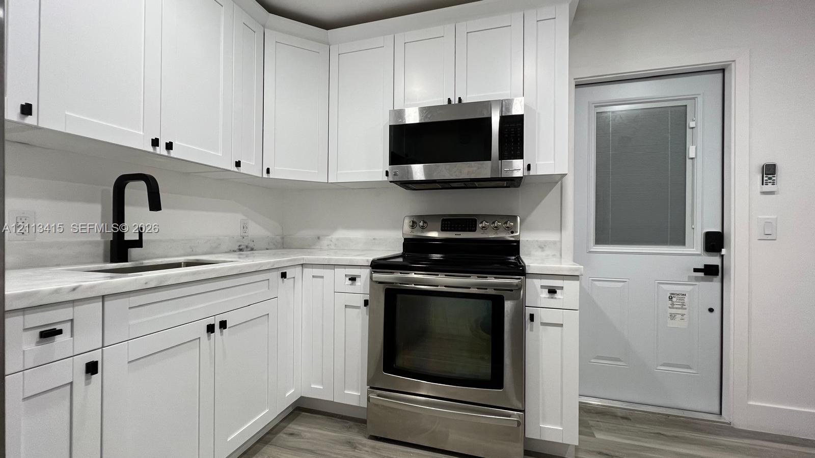 White shaker cabinetry, light-toned stone-finish countertops, stainless steel appliances, matte black hardware, and wood-finish flooring