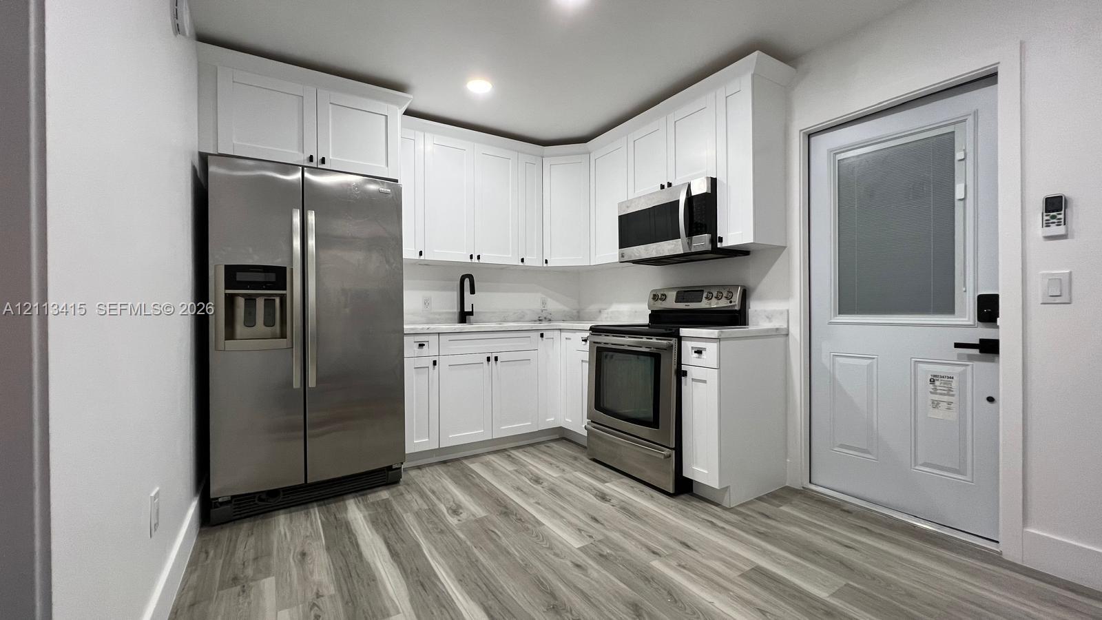 Kitchen featuring white shaker-style cabinetry, wood-finish flooring, stainless steel appliances, stone-finish countertops, and a high-arc matte black faucet Kitchen featuring white shaker-style cabinetry, wood-finish flooring, stainless steel appliances, stone-finish countertops, and a high-arc matte black faucet