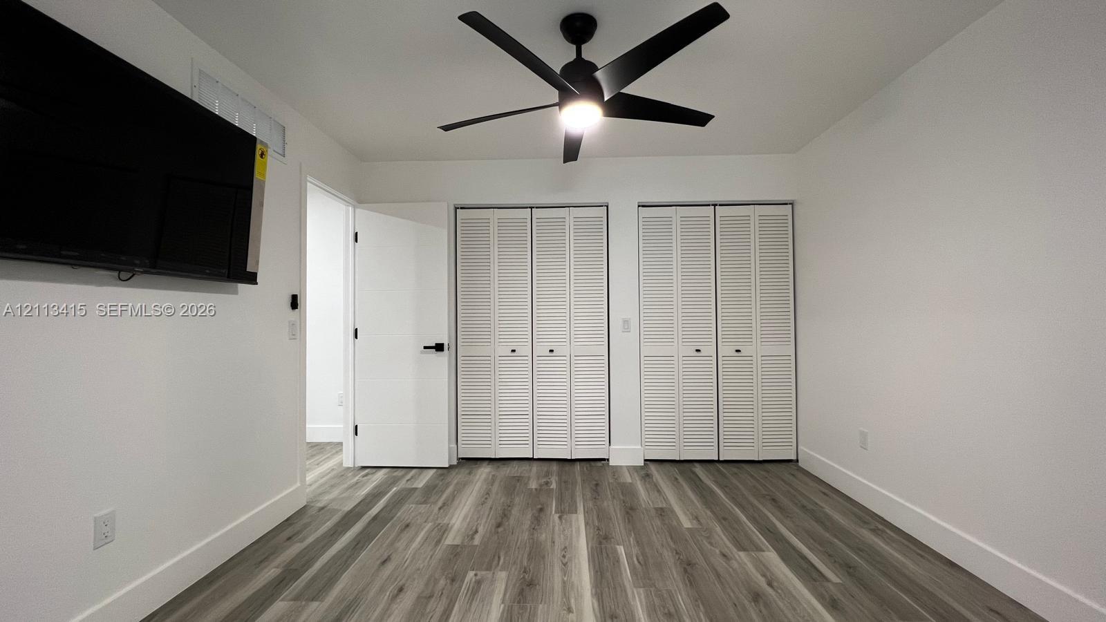 Wood-finish flooring, dual bi-fold louvered closets, matte black ceiling fan with integrated lighting, and matte black door hardware