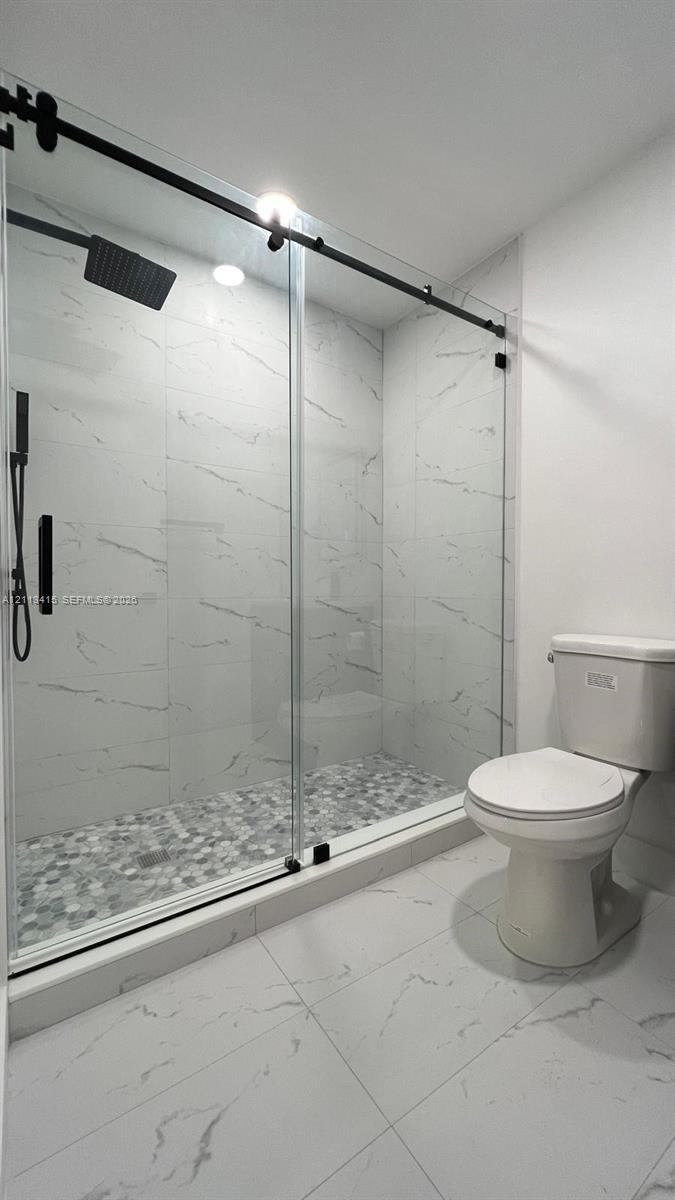 Walk-in shower featuring large-format stone-pattern tile walls, a pebble-finish floor, a matte black sliding glass enclosure, and a rainfall showerhead