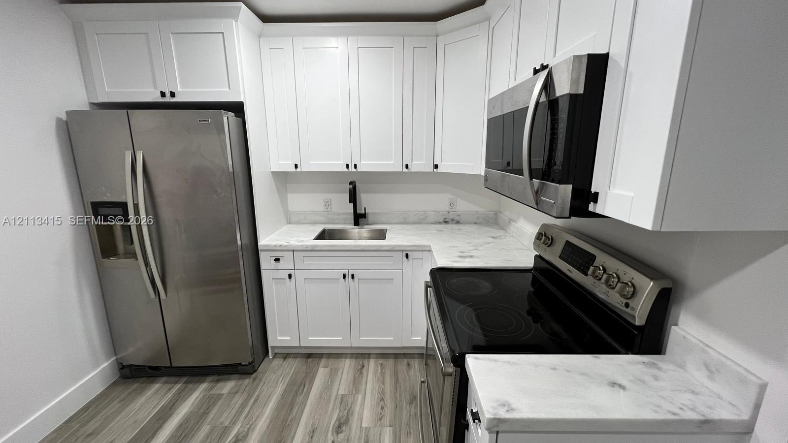 Kitchen featuring white Shaker-style cabinetry, stone-finish countertops, stainless steel appliances, a black pull-down faucet, and wood-finish flooring