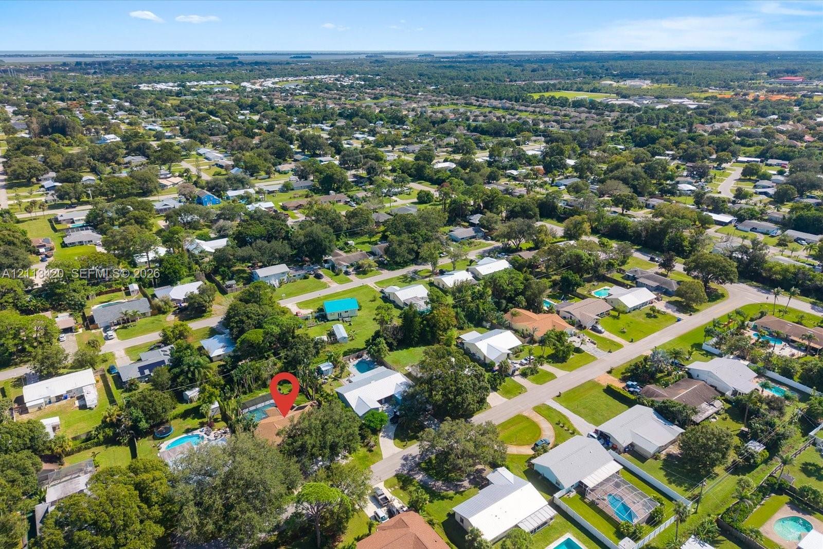 Aerial perspective of the residential property featuring a screened-in pool enclosure, mature canopy trees, and paved street access