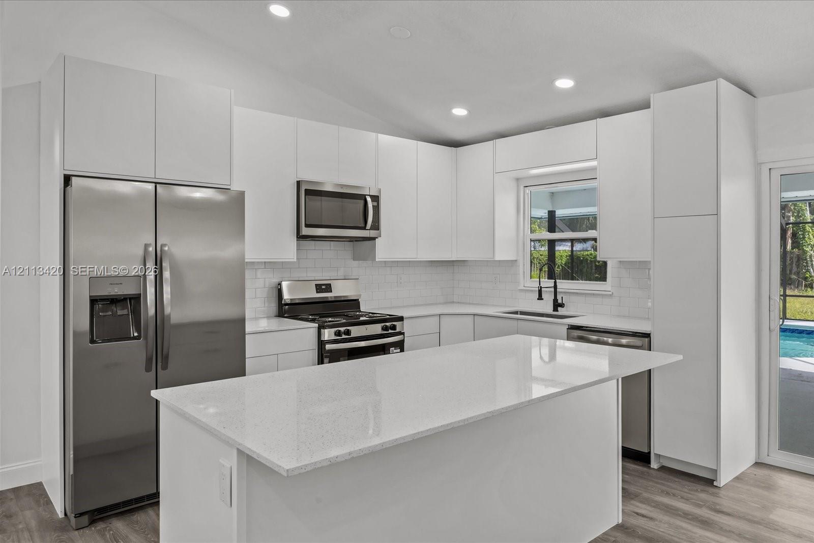 Kitchen featuring flat-panel white cabinetry, a center island with stone-finish countertops, stainless steel appliances, a white subway tile backsplash, and recessed lighting