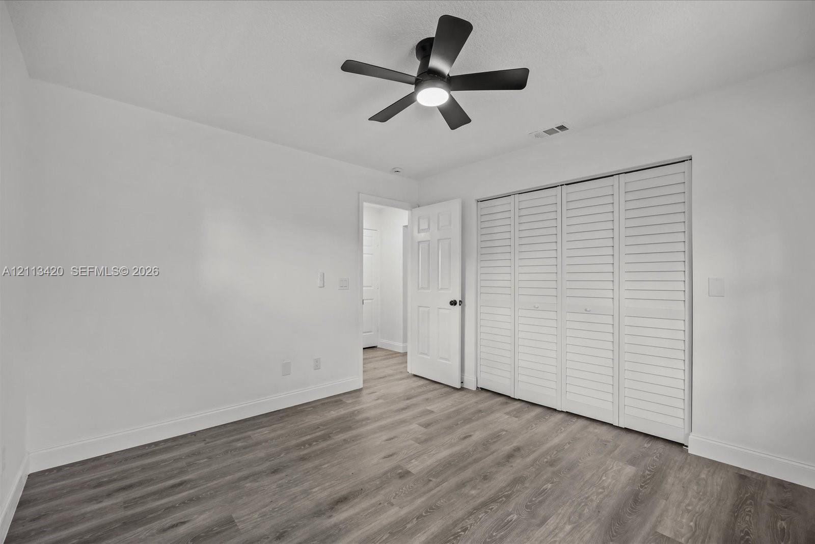 Interior space featuring wood-finish flooring, a matte black multi-blade ceiling fan with integrated light, and a four-panel louvered closet door
