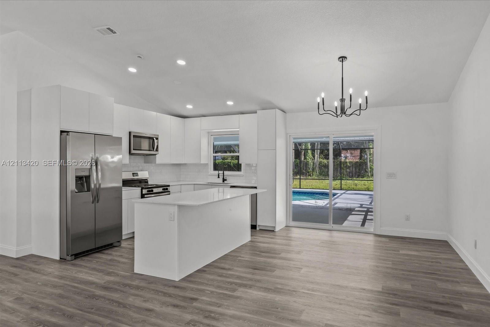 Kitchen featuring white cabinetry, quartz-surface center island, stainless steel appliances, wood-finish flooring, and sliding glass doors