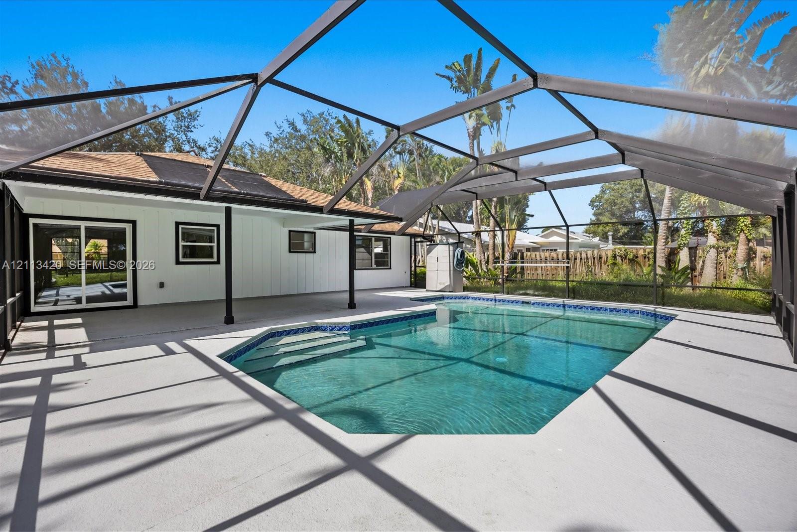 Screen-enclosed patio featuring a concrete pool deck, geometric swimming pool with built-in steps, and white exterior siding