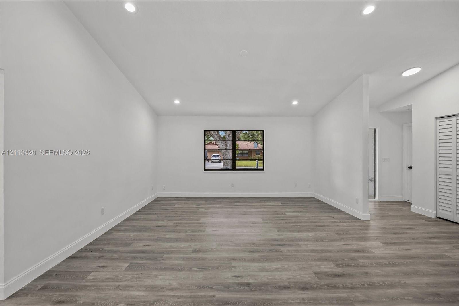 Neutral interior space featuring wood-finish flooring, recessed lighting, vaulted ceilings, and louvered closet doors