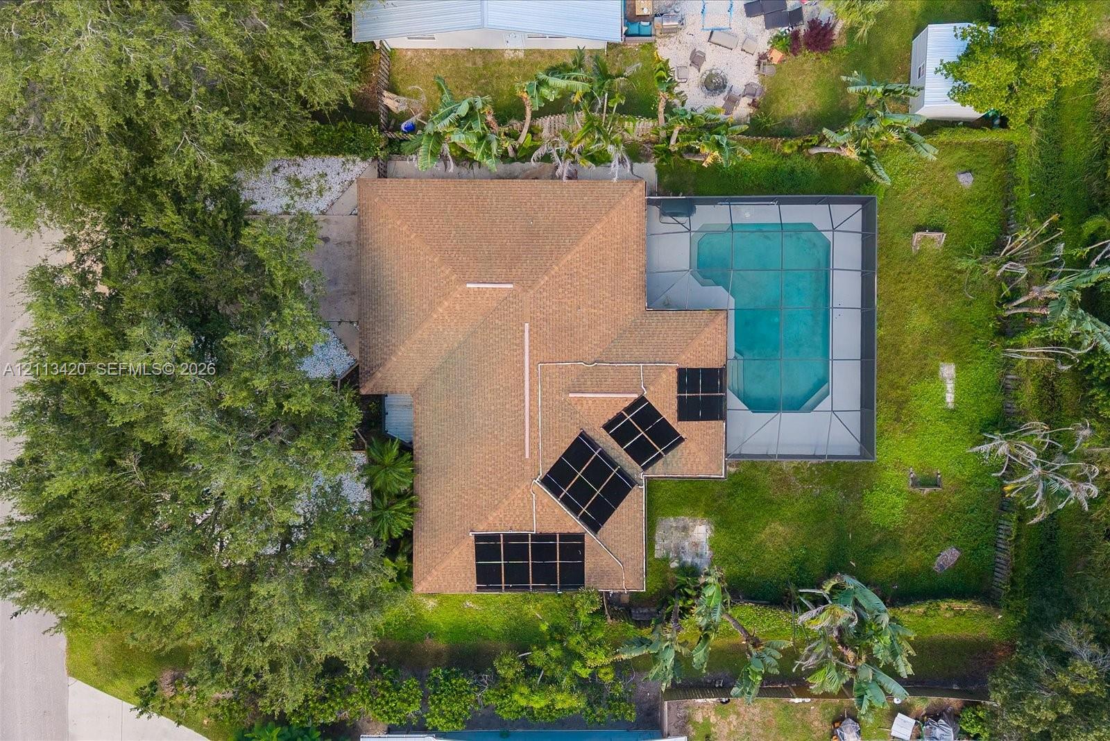 Aerial perspective featuring a shingled roof with installed solar panels, a screened-in swimming pool, and mature trees on the lot