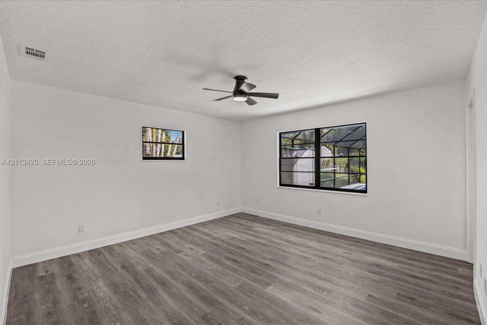 Room featuring wood-finish flooring, matte black window frames, and an integrated ceiling fan with light fixture