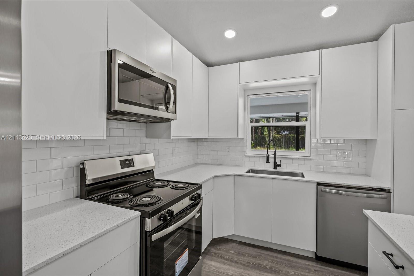Kitchen featuring white cabinetry, subway tile backsplash, stainless steel appliances, light-toned countertops, and wood-finish flooring