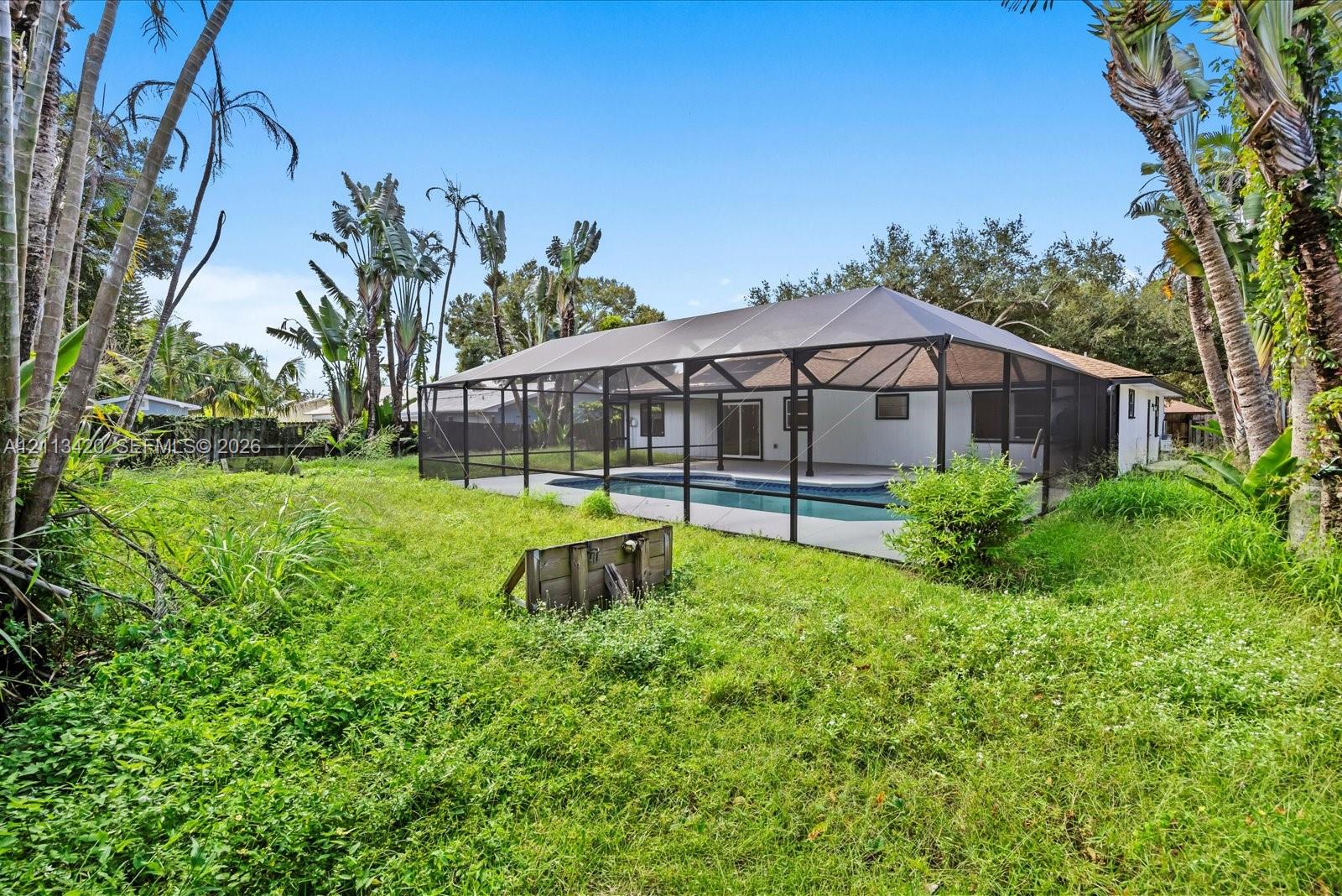 Screened-in patio area featuring a swimming pool and mature tropical landscaping