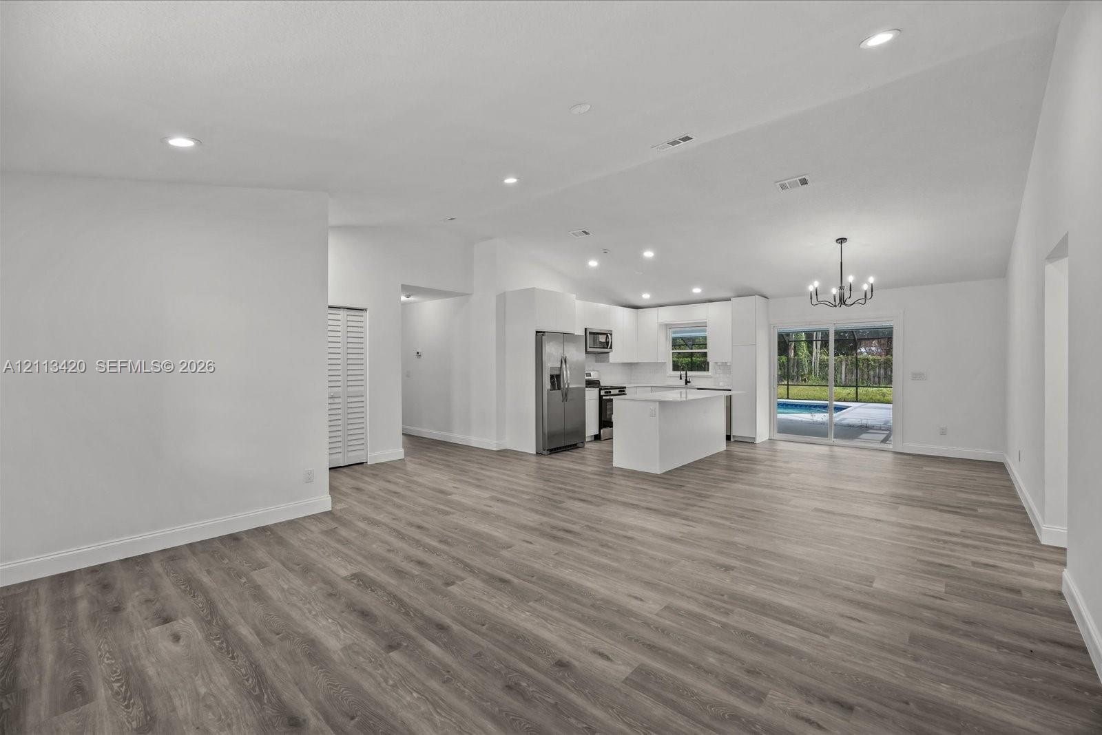 Open floor plan featuring vaulted ceilings, wood-finish flooring, recessed lighting, and a kitchen equipped with a center island and stainless steel appliances