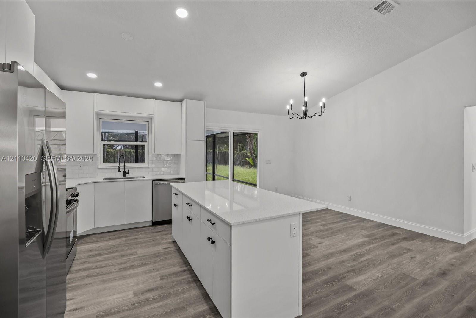 Kitchen featuring a central island with a solid surface countertop, white shaker-style cabinetry, stainless steel appliances, a modern chandelier, and wood-finish flooring