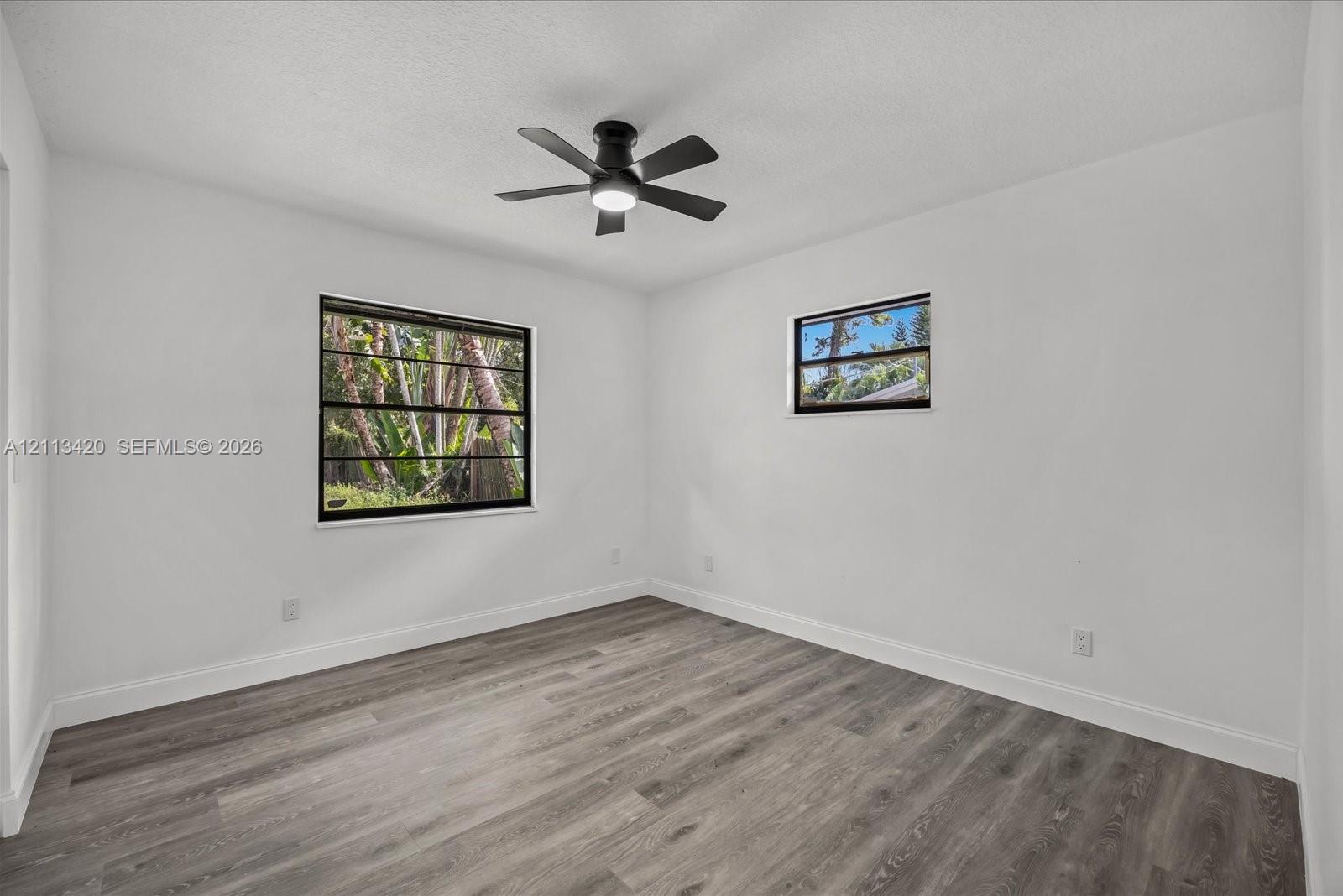 Room featuring wood-finish flooring, white walls, and a ceiling-mounted fan with integrated lighting