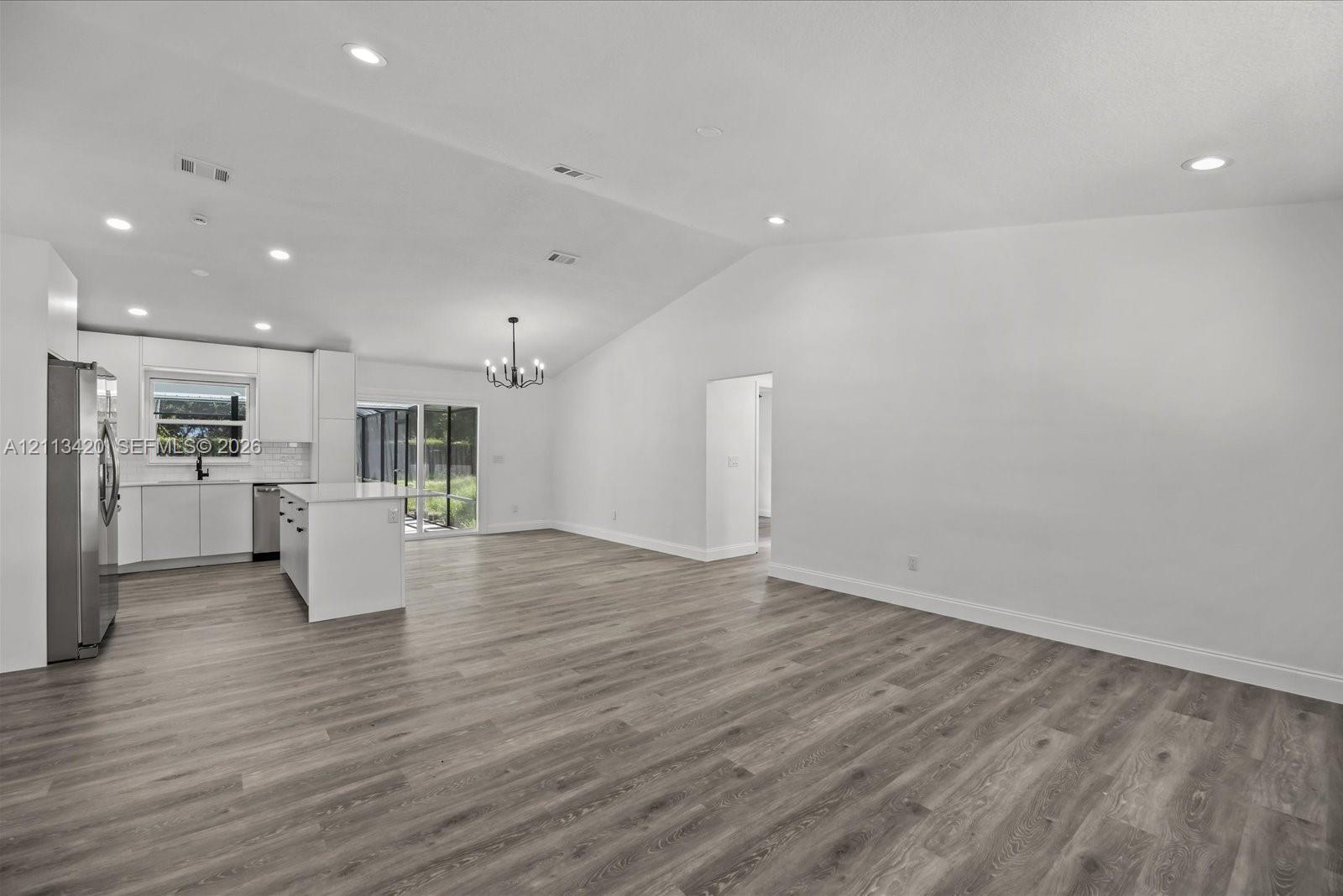 Open-concept interior featuring vaulted ceilings, recessed lighting, wood-finish flooring, and a kitchen with white cabinetry and a center island