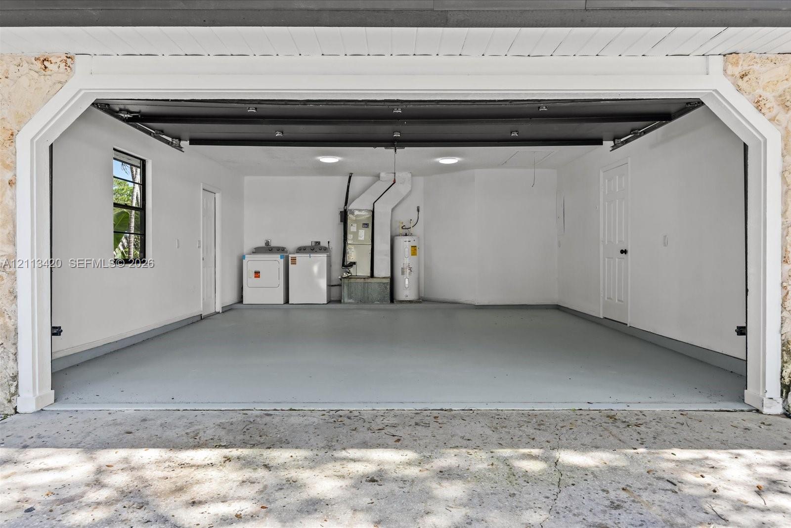 Two-car garage featuring a smooth-finish floor, white walls, dual flush-mount ceiling lights, and integrated laundry hookups