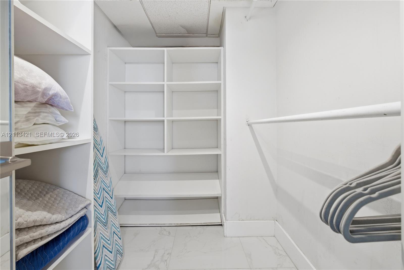 Walk-in closet featuring white built-in shelving, stone-finish flooring, and a horizontal hanging rod