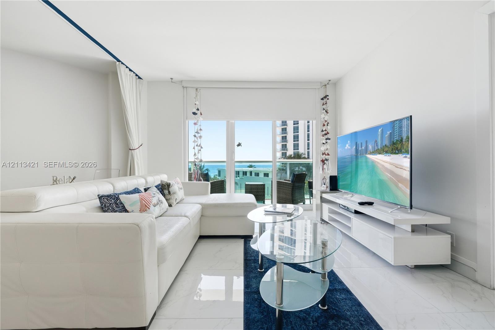 Living area featuring large-format tile flooring, wall-to-wall glass sliding doors, and a private balcony