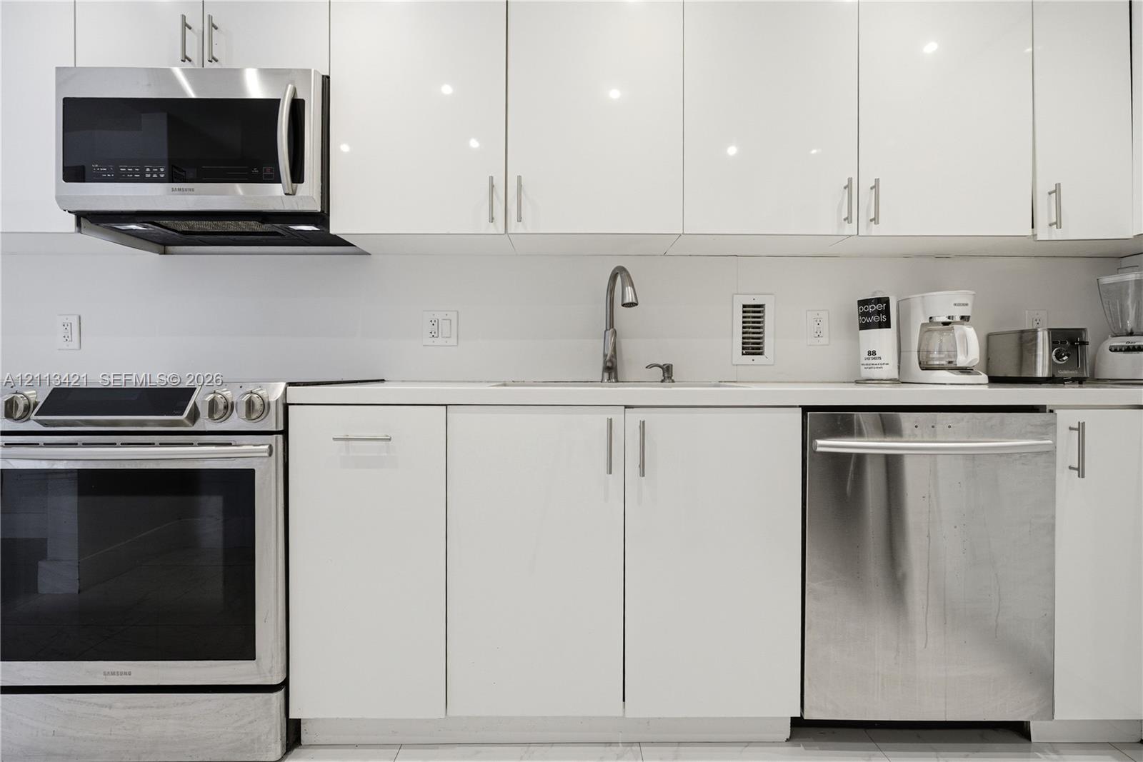 High-gloss white cabinetry, stainless steel appliances, solid surface countertops, and an undermount sink with a gooseneck faucet