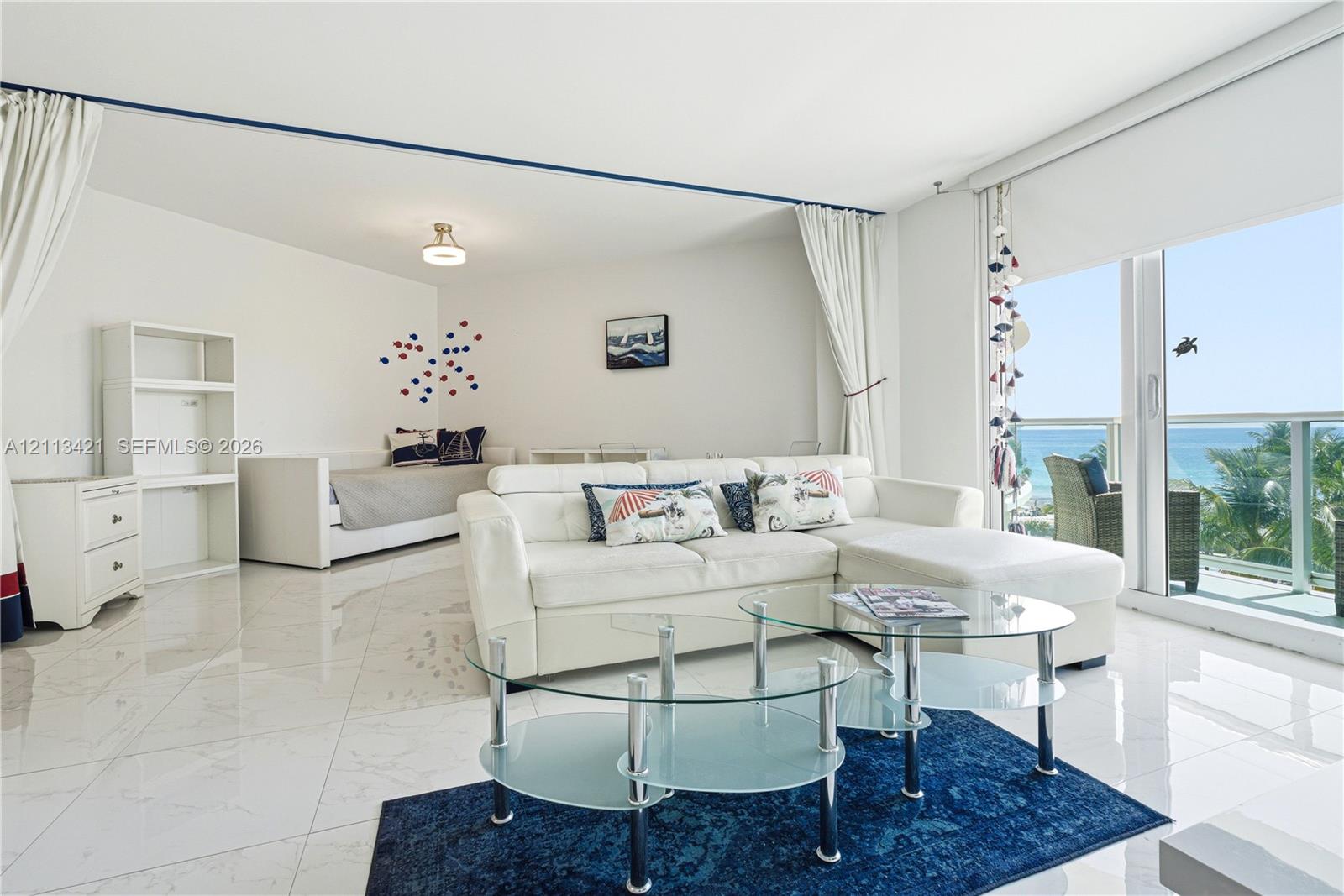 Polished tile flooring, built-in shelving unit, expansive sliding glass door, and private balcony with ocean backdrop