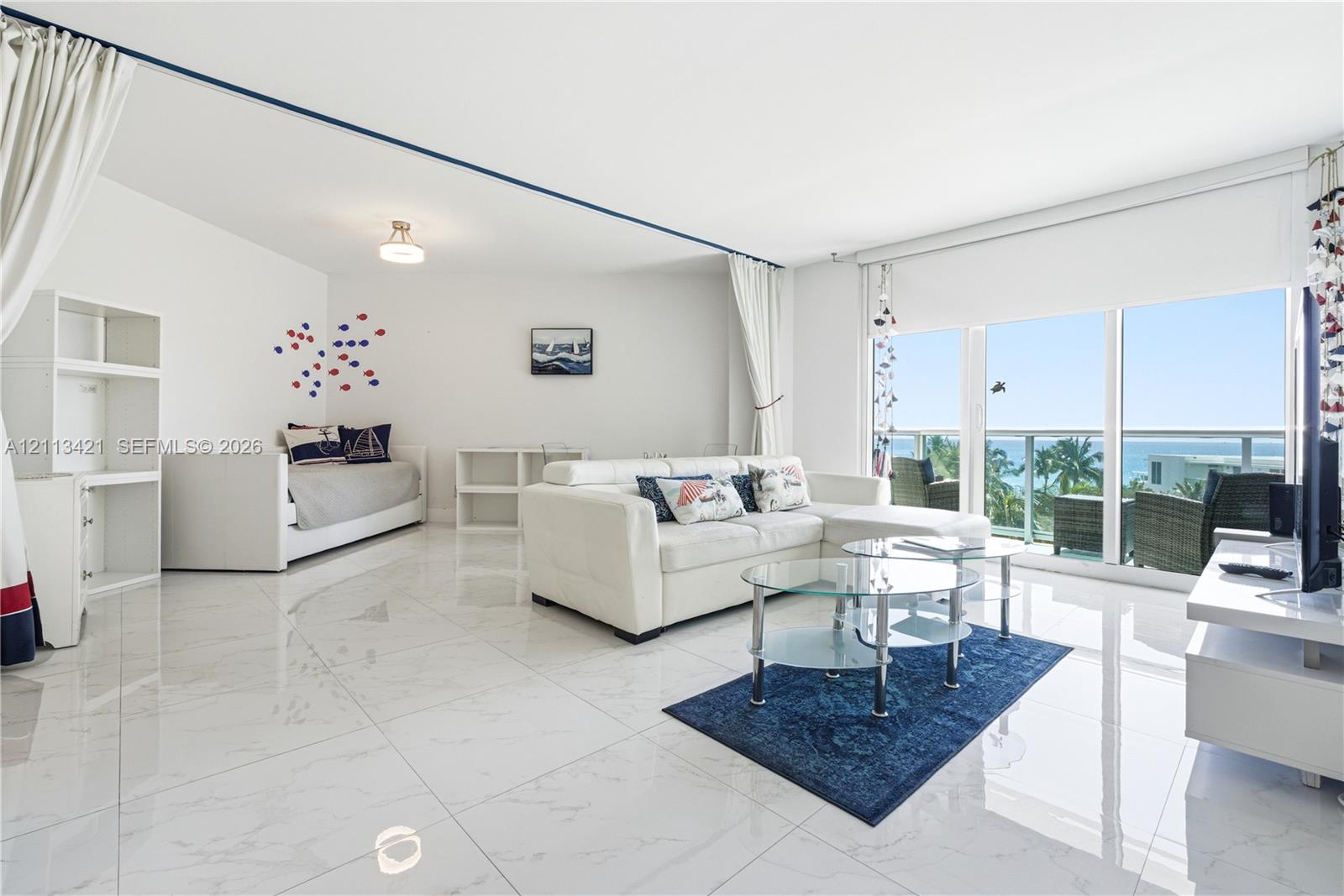 Large-format white tile flooring, floor-to-ceiling sliding glass doors, and a private balcony featuring a glass railing