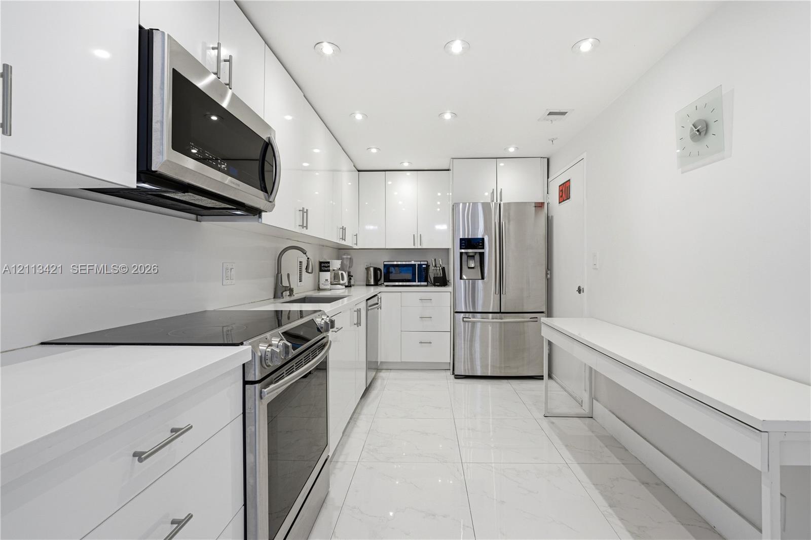 Contemporary kitchen featuring high-gloss white cabinetry, stainless steel appliances, solid-surface countertops, recessed lighting, and tile flooring