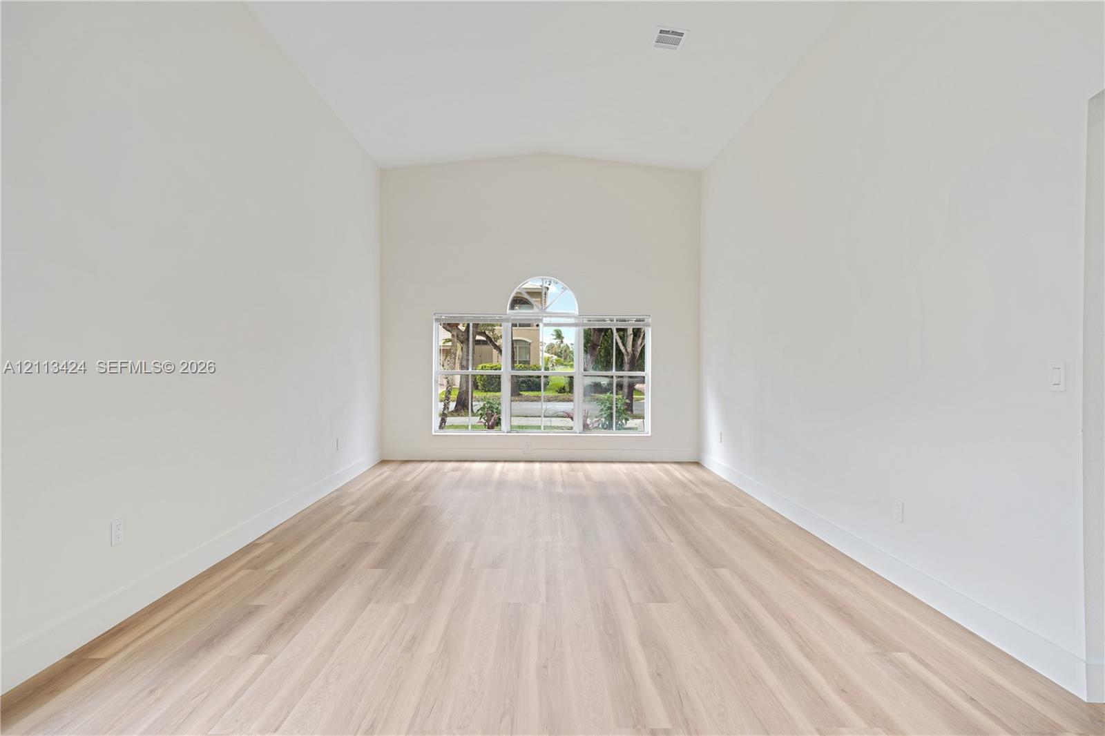 Vaulted ceiling featuring a multi-paned window with an arched transom, complemented by light-toned wood-finish flooring