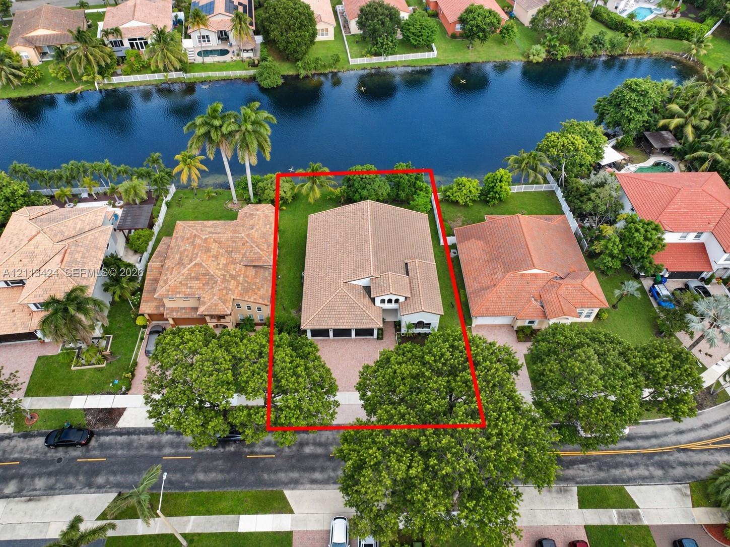 Waterfront residential property featuring a tiled roof, multi-car garage, brick-paver driveway, and a spacious backyard