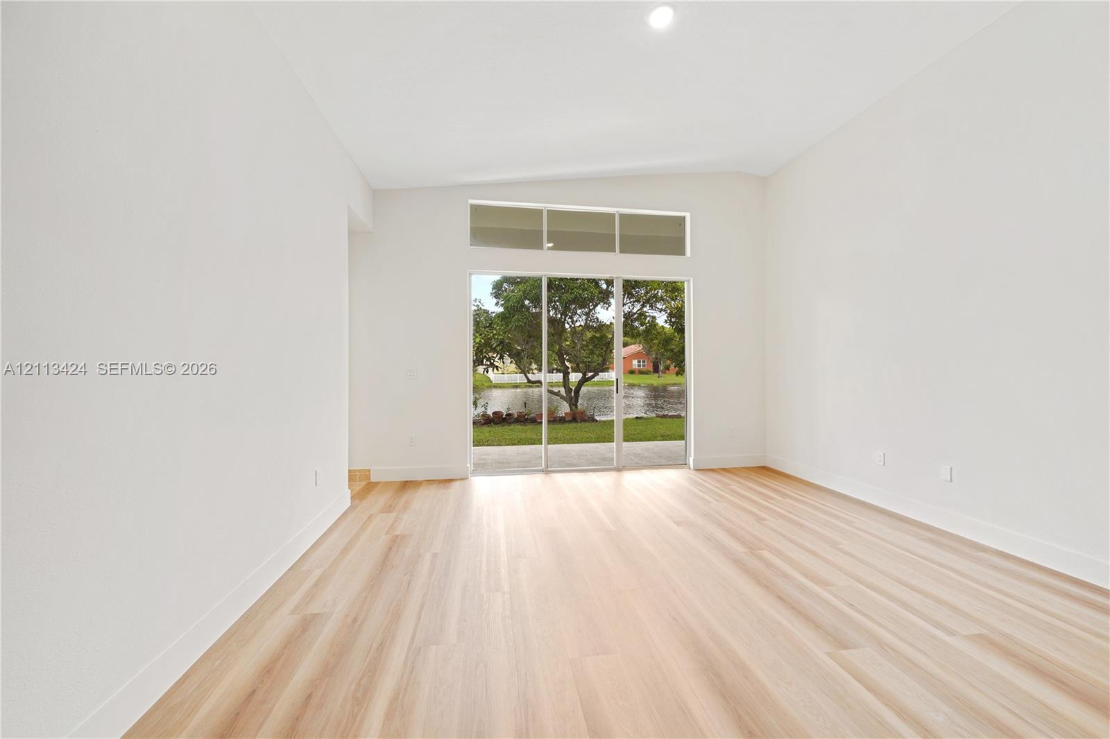 Interior space featuring vaulted ceilings, light-toned wood-finish flooring, and expansive sliding glass doors topped with rectangular transom windows