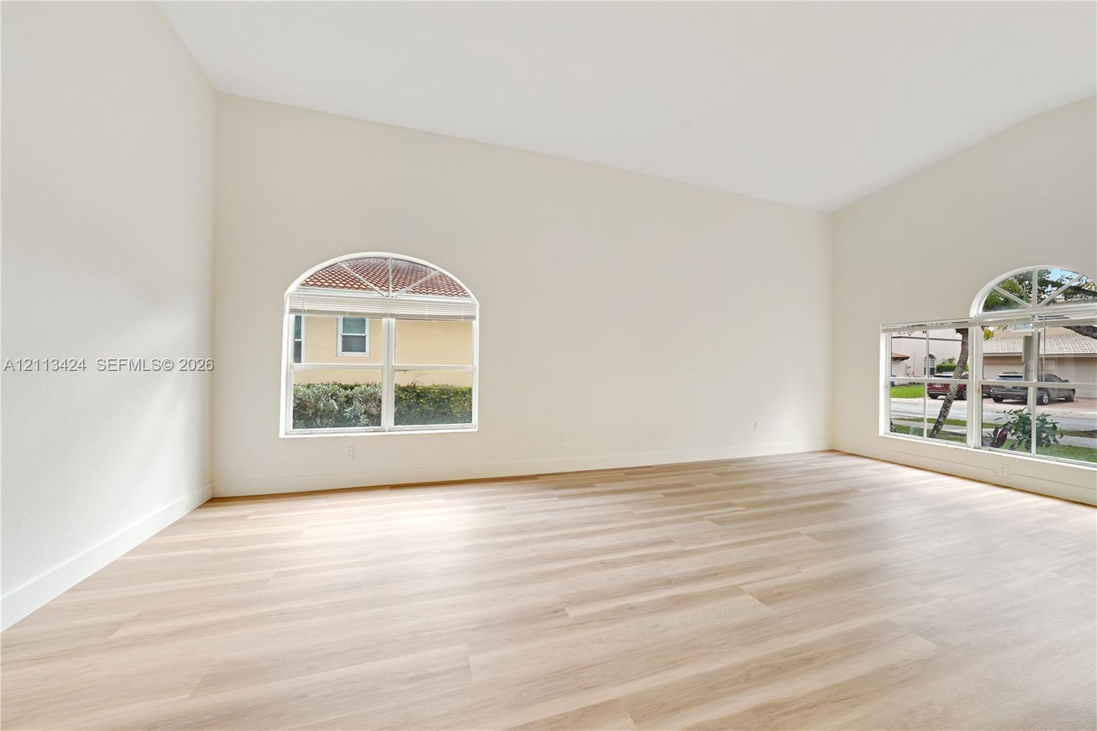 Spacious interior featuring vaulted ceilings, neutral wall tones, wood-finish flooring, and arched windows