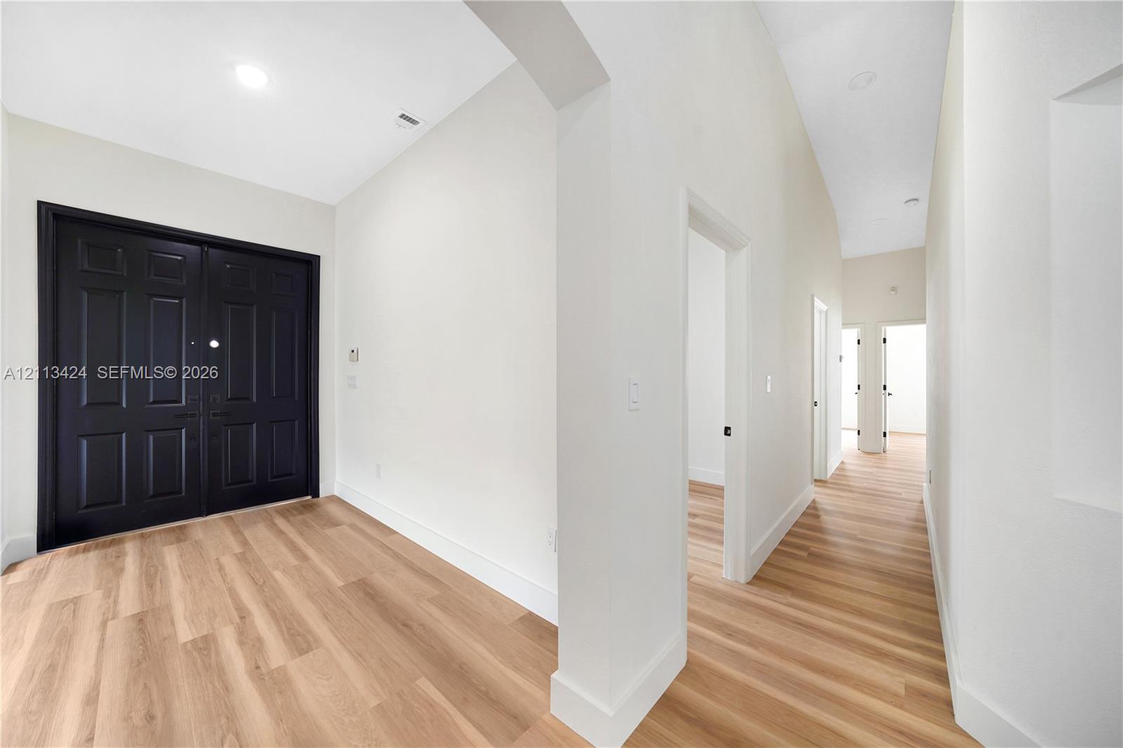 Entryway featuring double black doors, high ceilings, wood-finish flooring, recessed lighting, and an arched architectural opening