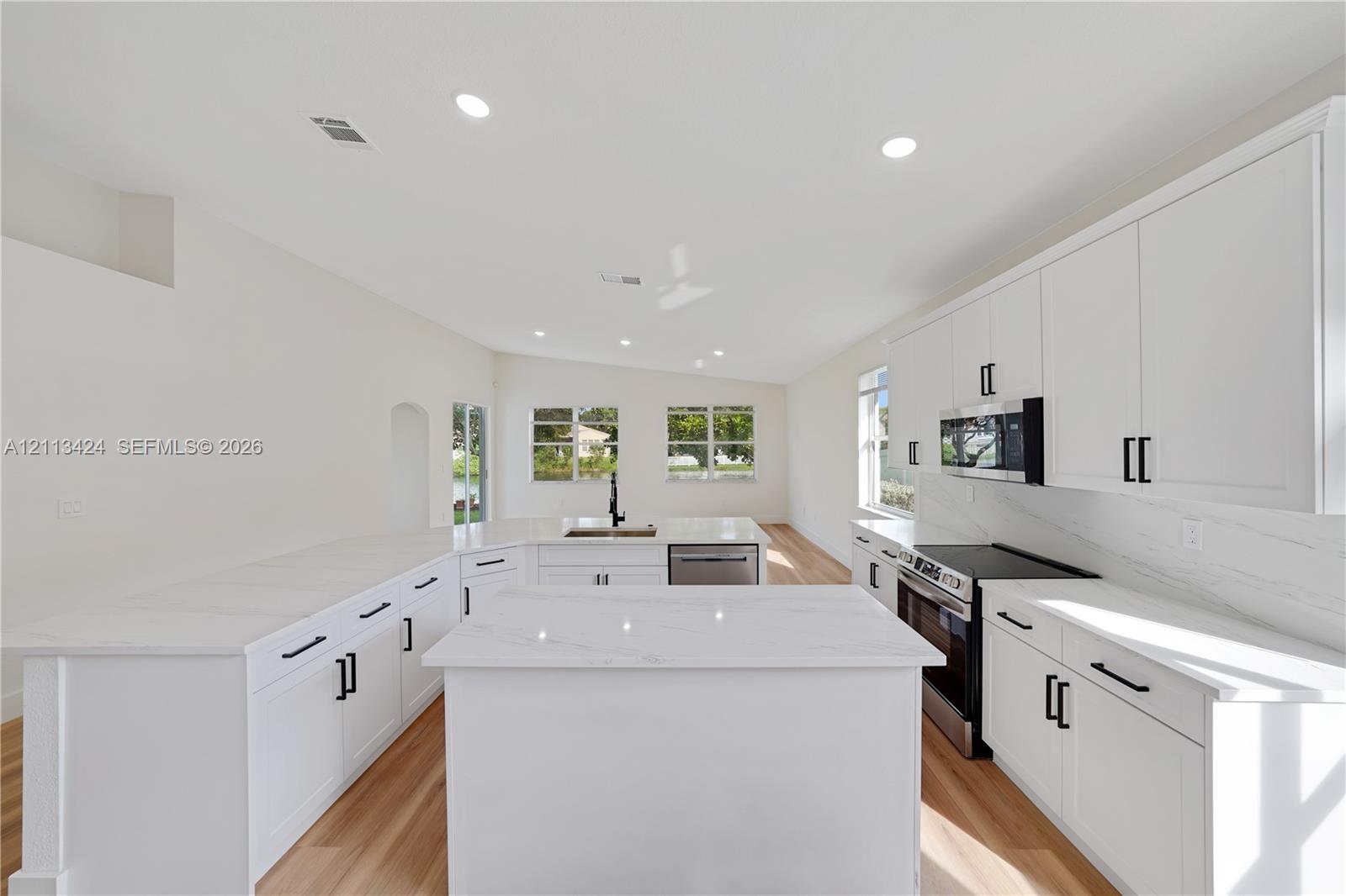 Kitchen featuring white shaker-style cabinetry, quartz countertops with a waterfall-edge center island, integrated stainless steel appliances, and wood-finish flooring