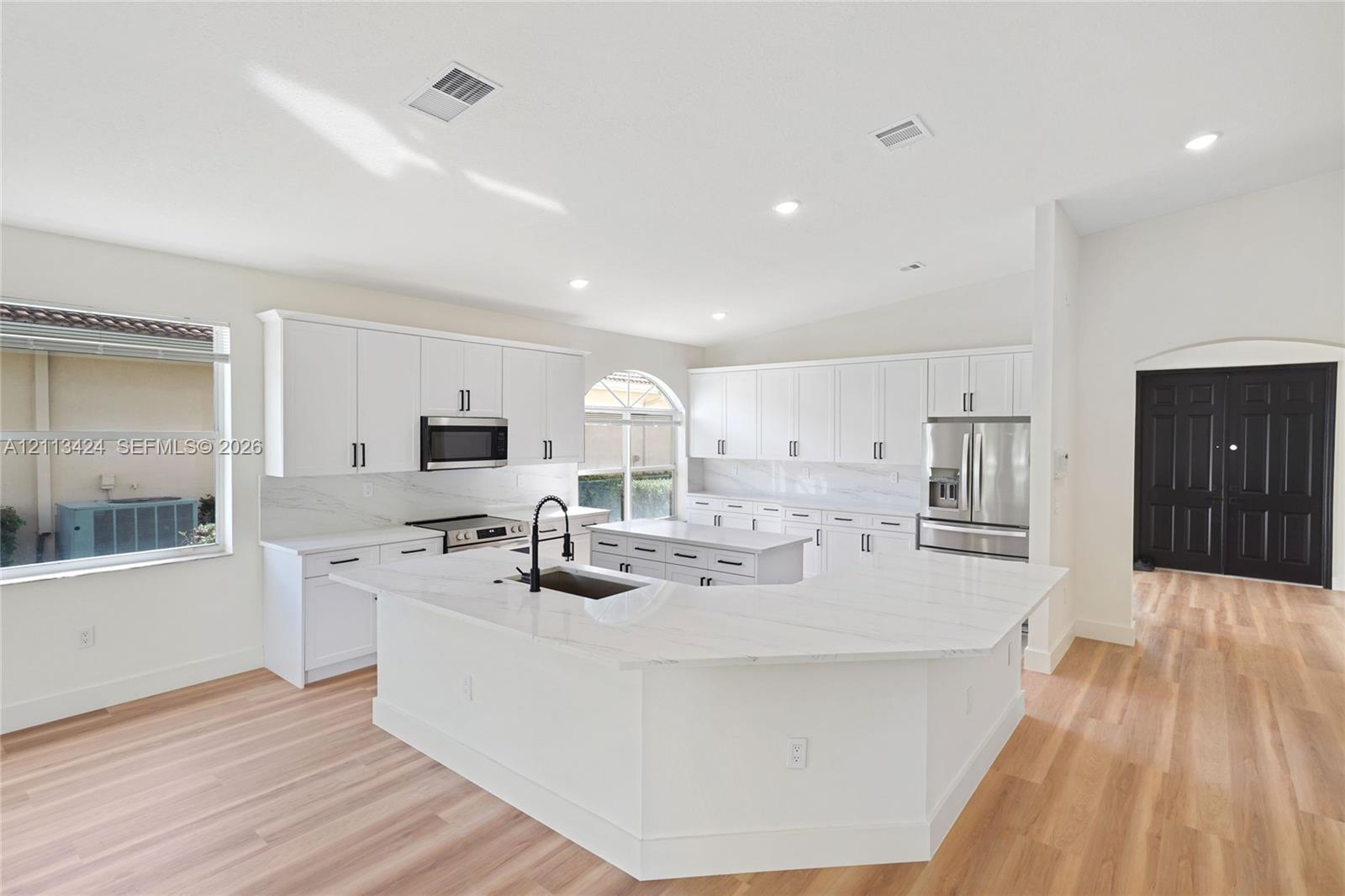 Kitchen featuring white shaker-style cabinetry, quartz countertops with a waterfall edge island, stainless steel appliances, and wood-finish flooring