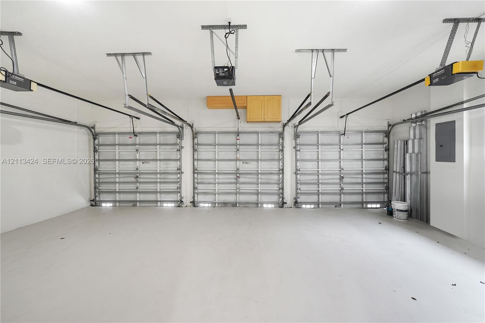 Three-car garage featuring finished concrete flooring, three overhead door tracks, ceiling-mounted automatic door openers, and wall-mounted cabinetry
