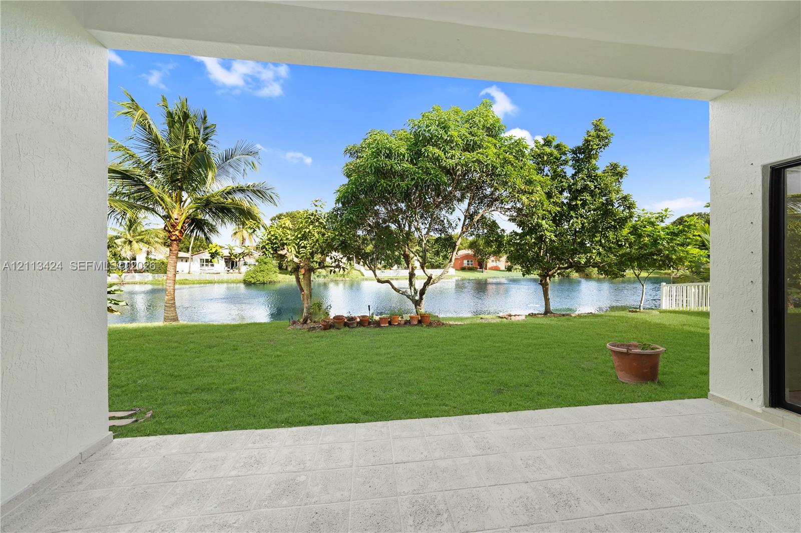 Covered patio with tile flooring featuring expansive water frontage, a manicured lawn, and mature trees