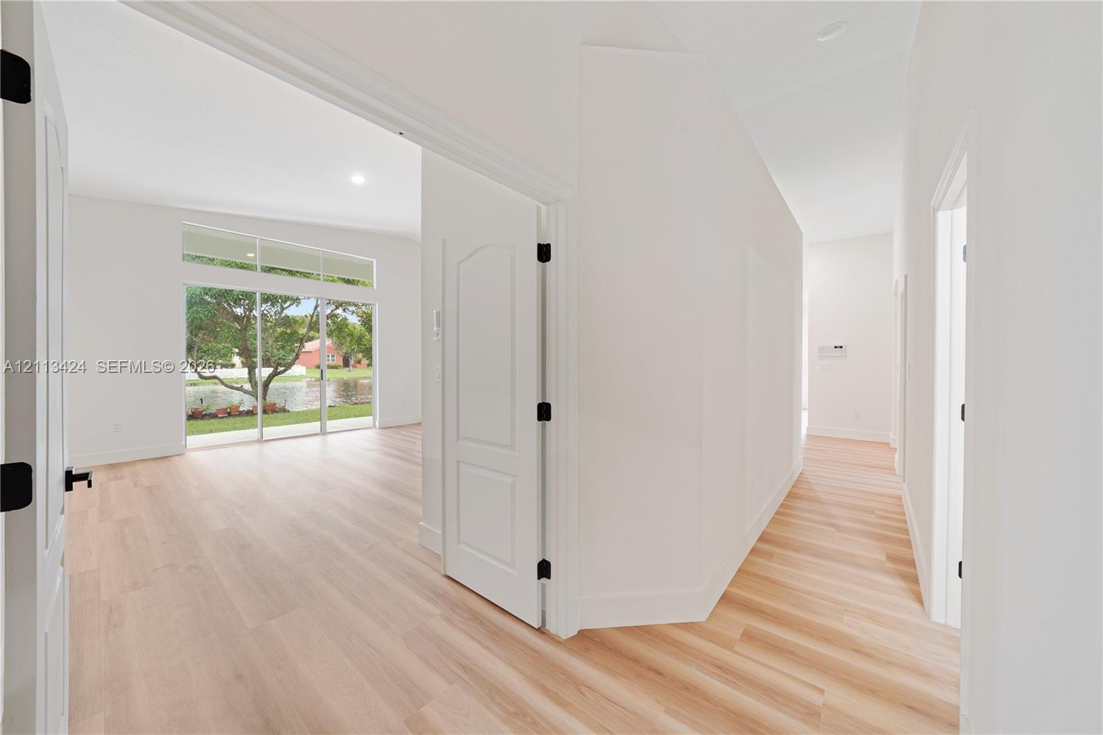 Interior featuring light-toned wood-finish flooring, high ceilings, arched-top interior doors with matte black hardware, and floor-to-ceiling glass sliding doors