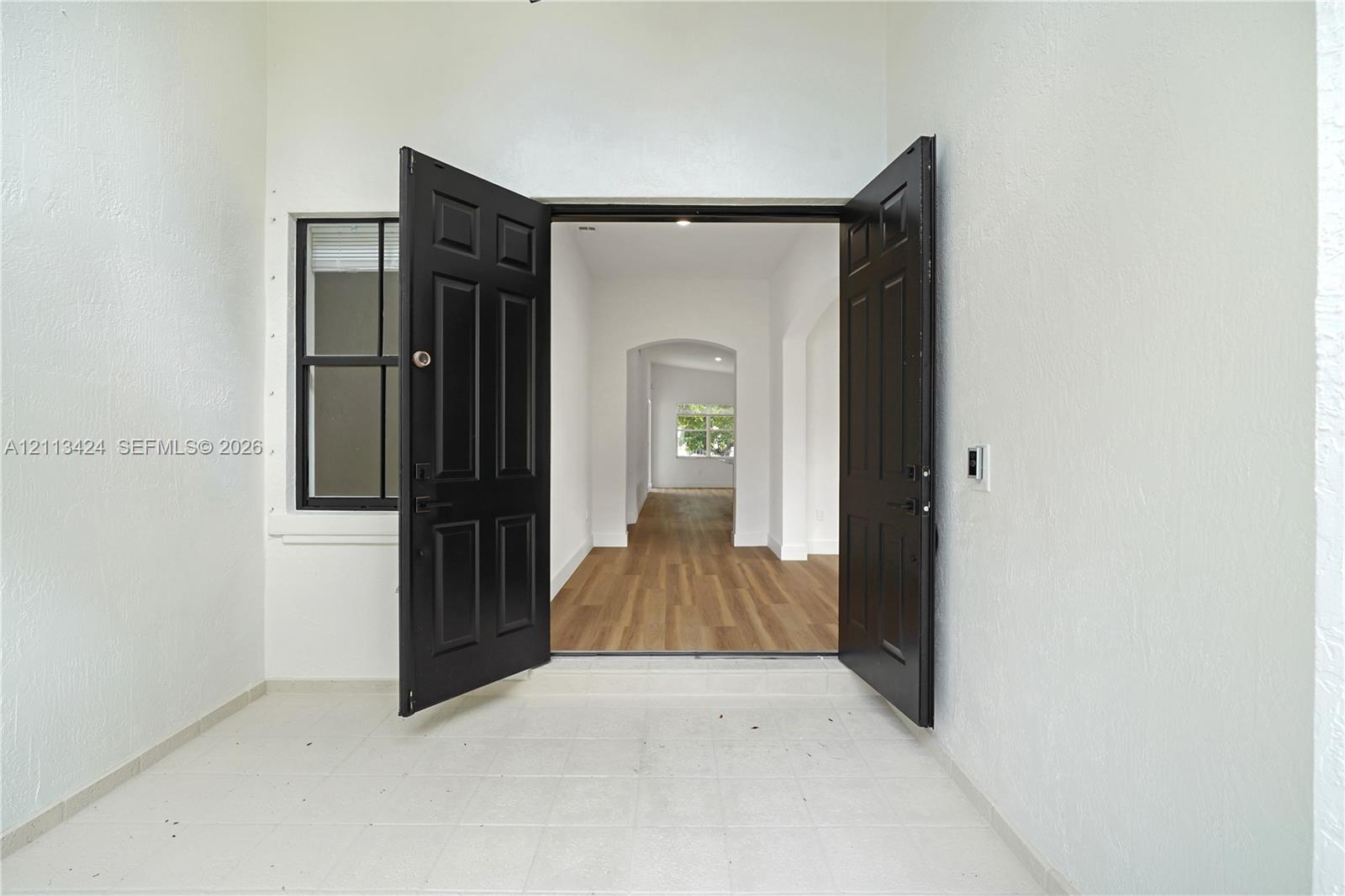 Double front entry doors with black finish, white textured wall exterior, single-pane side window, and interior wood-finish flooring