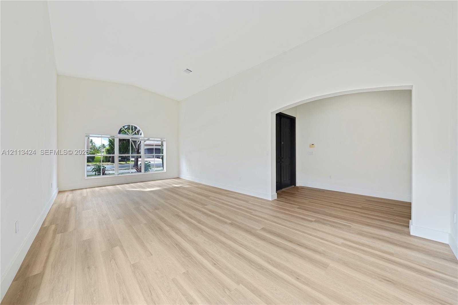 Vaulted ceilings, wood-finish flooring, and an arched entryway featuring a dark-finish door